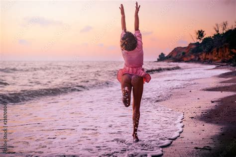 Silhouette of a girl in a pink dress on the beach, on the background of a pink dawn running ...