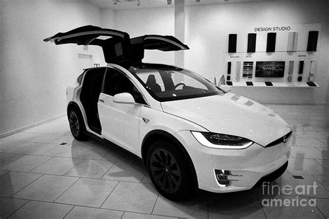 white Tesla Model X with falcon wing doors open during celebration display in a tesla gallery ...