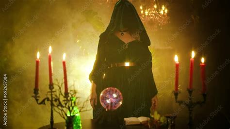 Fantasy woman witch undresses, removes hood that hides face creates magic, dark gothic room full ...