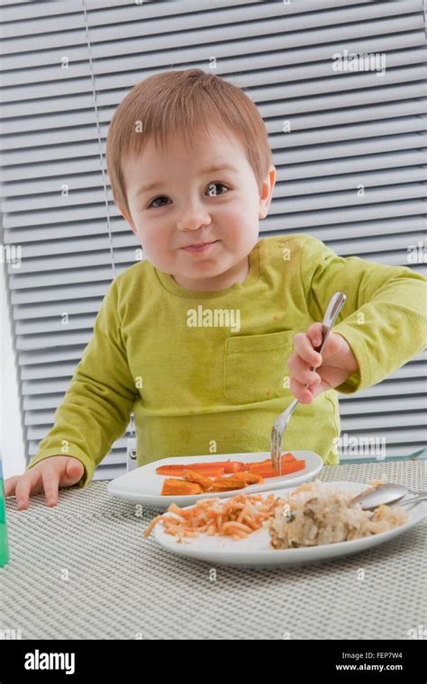 Baby boy feeding himself at dining table Stock Photo - Alamy