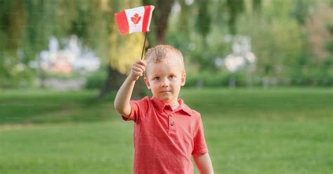Caucasian child boy holding waving Canadian flag outdoor. Kid child citizen celebrating Canada ...