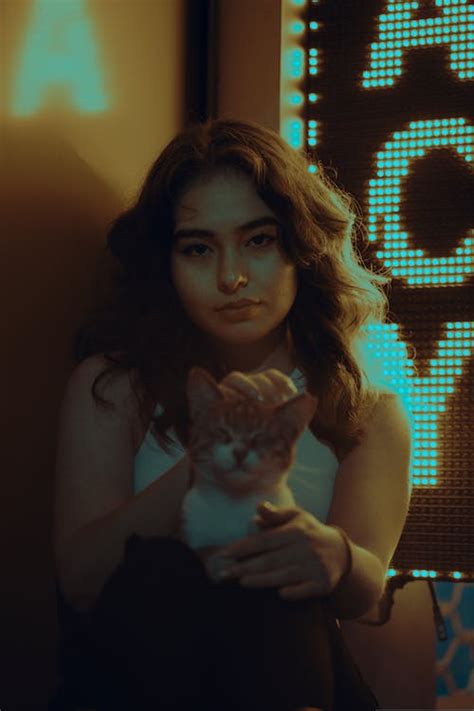 Young Woman Holding a Cat and Sitting by a LED Sign · Free Stock Photo