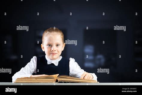 Smiling little girl sitting at desk with open book Stock Photo - Alamy