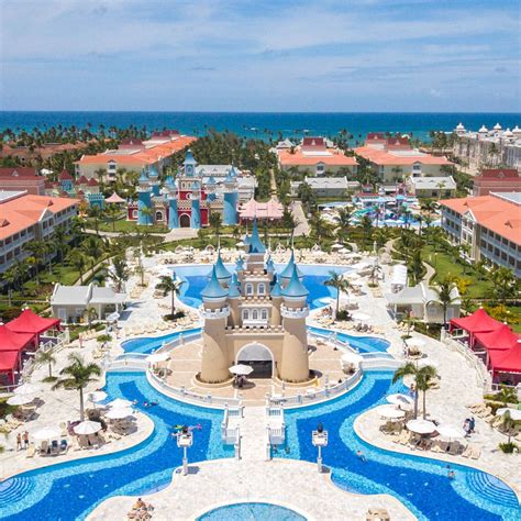 an aerial view of the resort and pool area with blue water, white sand and red umbrellas