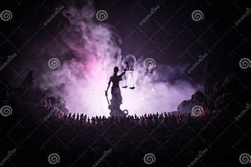 Silhouette of Blurred Giant Lady Justice Statue with Sword and Scale Standing Behind Crowd at ...
