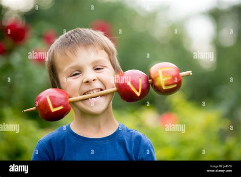 Cute little child, boy, holding a love sign, made from apples, letter graved in the apple ...
