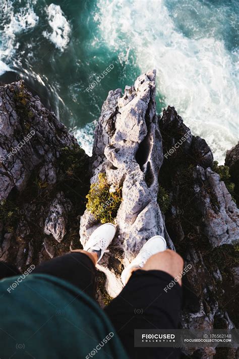 Looking down view of man standing on edge of cliff over tough sunlit ...