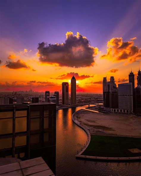 the sun is setting over a city with tall buildings in the foreground and a river running through it