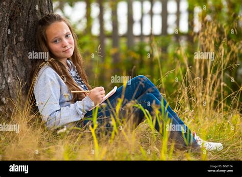 Beautiful teen-girl writing in a notebook while sitting in the park (looks into the camera Stock ...