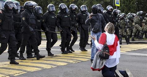 A woman covered herself by an old Belarusian national flag kneels in ...