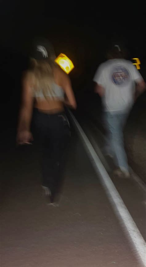 blurry photograph of people walking down the street at night time, with one person wearing a ...