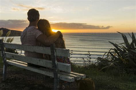 Couple in love sitting on bench looking at sunset stock photo