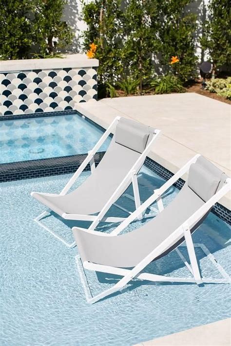 White and gray pool loungers sit on a tanning ledge in an in-ground ...