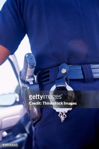 Closeup Of Hip Of Policeman With Gun And Handcuffs Hanging From Belt Inside Of Car Door In ...