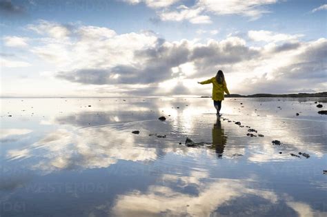 Woman walking amidst sea with reflection in Hvalnes Nature Reserve ...