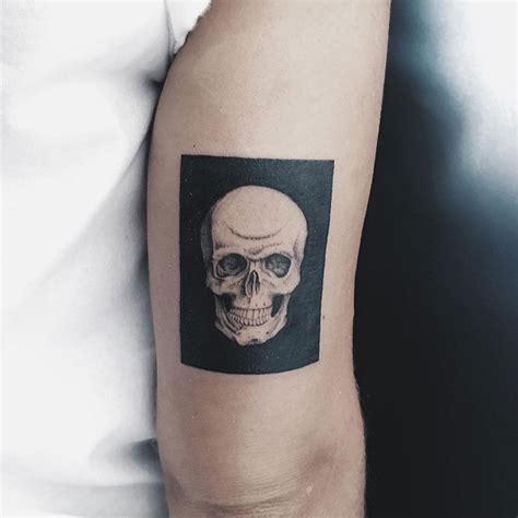 Realistic white skull tattoo inked in the solid black rectangle on the right upper arm above the ...