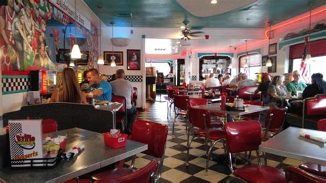 people sitting at tables in a diner with checkered flooring and red booths,