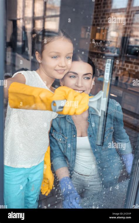 Happy mother and daughter in protective gloves cleaning window together ...