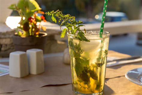 Alcoholic Drink Mojito, with fresh mint leaves, ice cubes and green straw, on an outside table ...