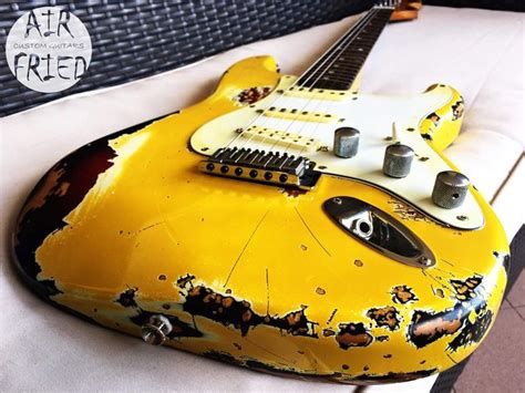 an old yellow electric guitar sitting on top of a white sheet covered bed with black and red ...