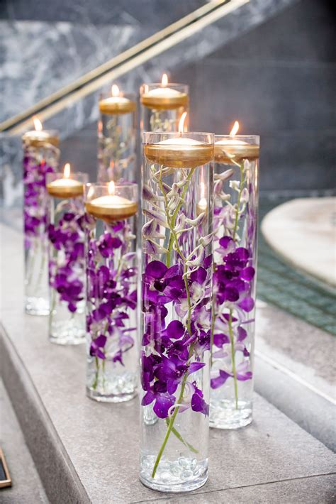 Glass vases were filled with purple orchids and floating gold candles for a… | Wedding flower ...