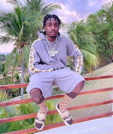 a man sitting on top of a wooden rail next to palm trees and wearing socks