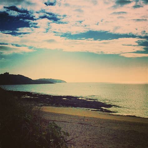 an ocean view with clouds in the sky and sand on the beach near water's edge