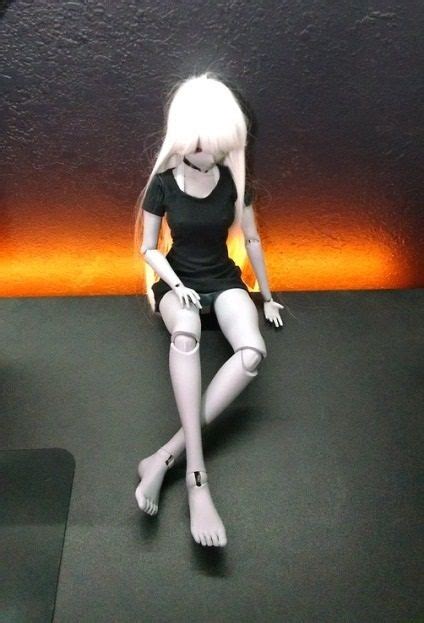 a white doll sitting on top of a black floor next to a wall with an orange light behind it