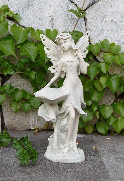 a statue of a fairy holding a flower in front of some ivys and stone wall