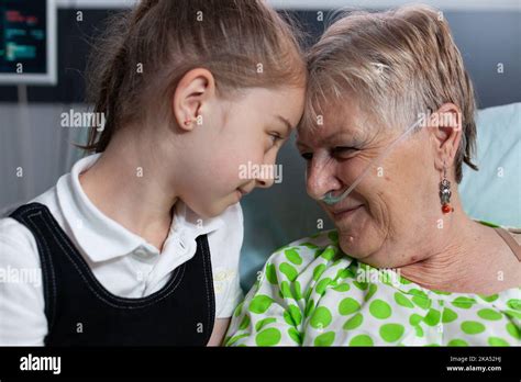 Elderly woman lying in hospital bed with breathing aids showing affection to little girl ...