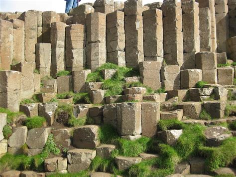 a man standing on top of a large rock formation with grass growing in between it