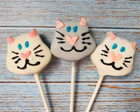 three cat lollipops are sitting on a blue wooden table with white and pink frosting