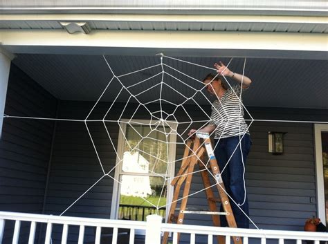 a man standing on top of a wooden ladder next to a spider web covered house