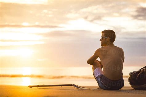 Man sitting on beach at sunrise stock photo