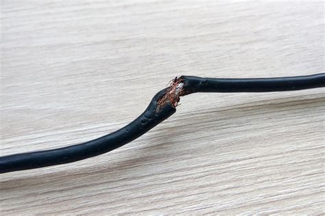 Damaged black electric cord on white background. Dangerous broken power electrical cable ...