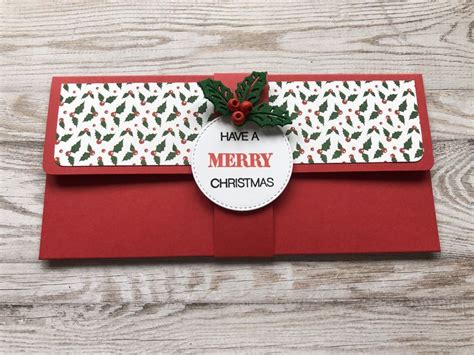 a red envelope decorated with holly leaves and a merry tag