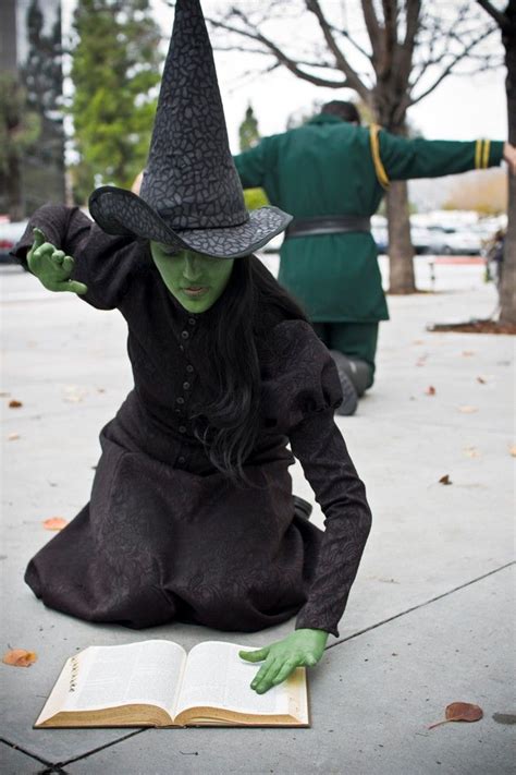 a woman in a witch costume sitting on the ground with an open book next ...