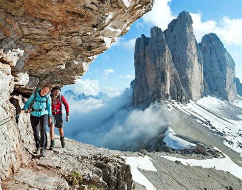 two people hiking up the side of a mountain with snow and clouds in the ...