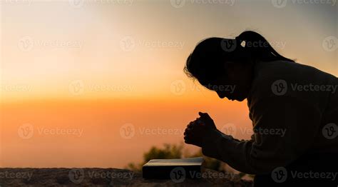 Silhouette of woman kneeling down praying for worship God at sky background. Christians pray to ...