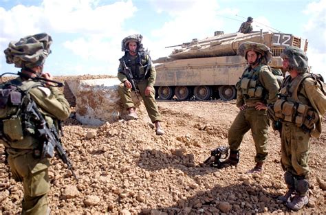 Israeli soldiers wearing Mitznefet helmet cover. Merkava Mk 4 tank visible at the background ...