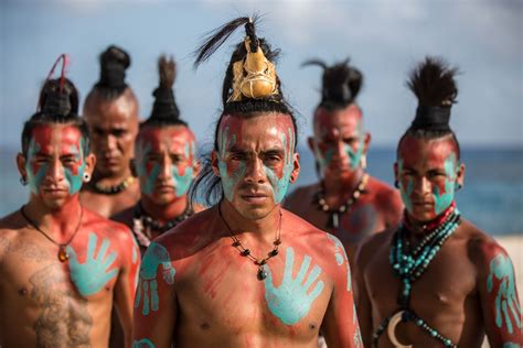 a group of men with painted hands on their faces and body, standing in front of the ocean