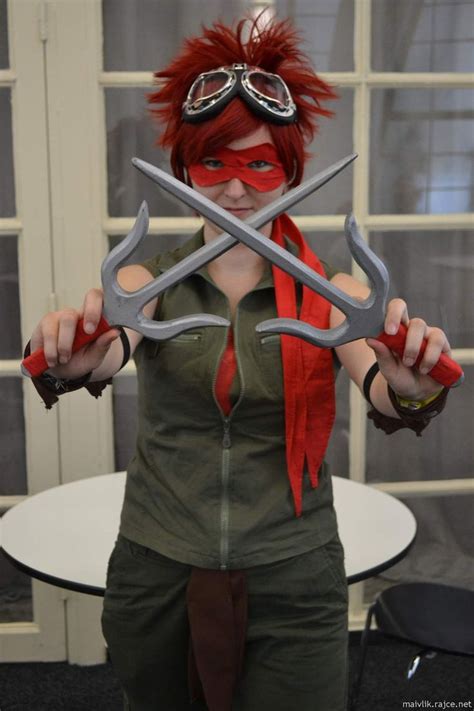 a woman with red hair and goggles holding two large scissors in front of her face