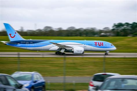 a blue and white jet airliner taking off from an airport runway with cars parked on the tarmac