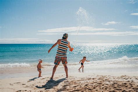 Kids playing with water at the beach with their dad on a sunny day ...