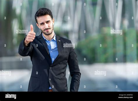 Young businessman wearing suit showing thumbs up while standing outdoors Stock Photo - Alamy