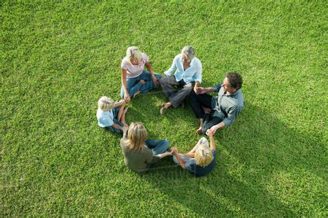 People sitting in circle on grass holding hands - Stock Photo - Dissolve