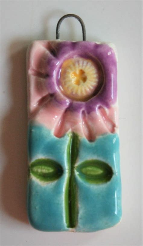 a ceramic flower is hanging from a hook on a white wall with green leaves and purple petals
