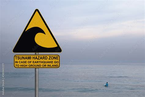 Tsunami warning and evacuation sign located on a beach. Blue calm sea misty landscape and only ...