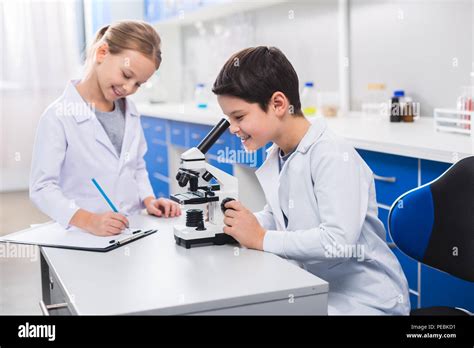 Observación Científica. Inteligente niño lindo positivo de pie juntos en el laboratorio y el ...