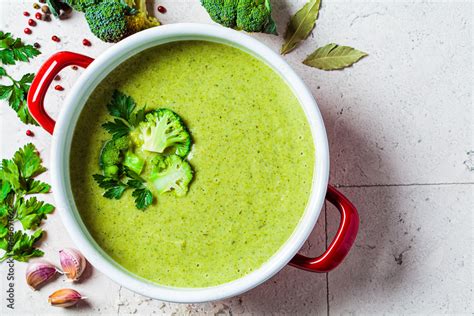 Broccoli soup puree in red saucepan on gray tile background with ...